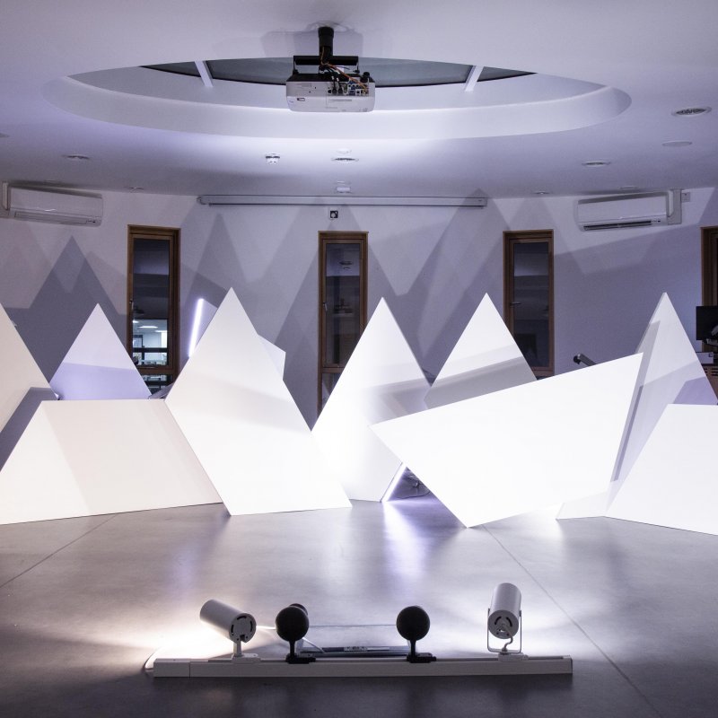 White triangle sculptures in a room lit with purple light