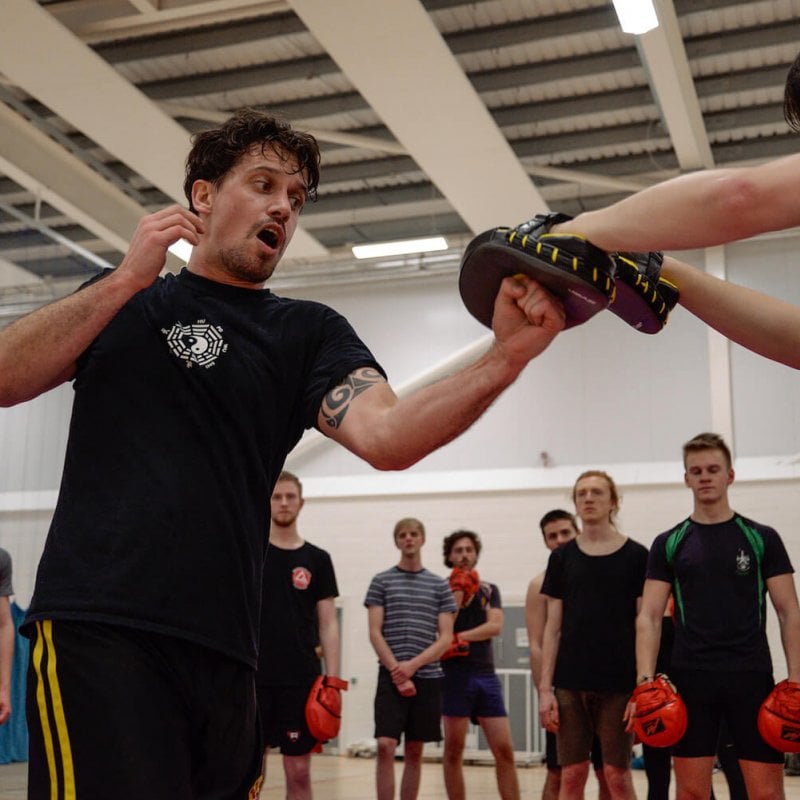 Falmouth University student striking up with fist into boxing pads.