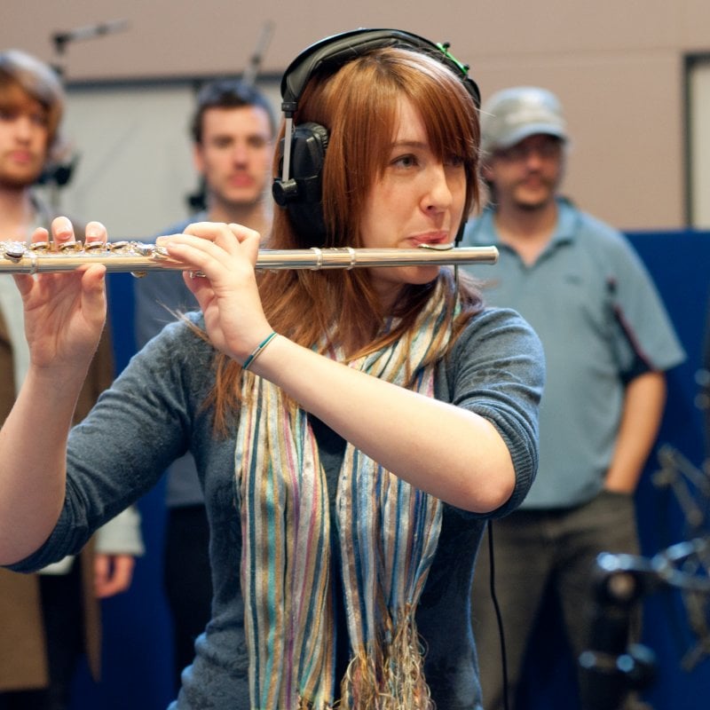 Girl with headphones on playing flute in recording studio.