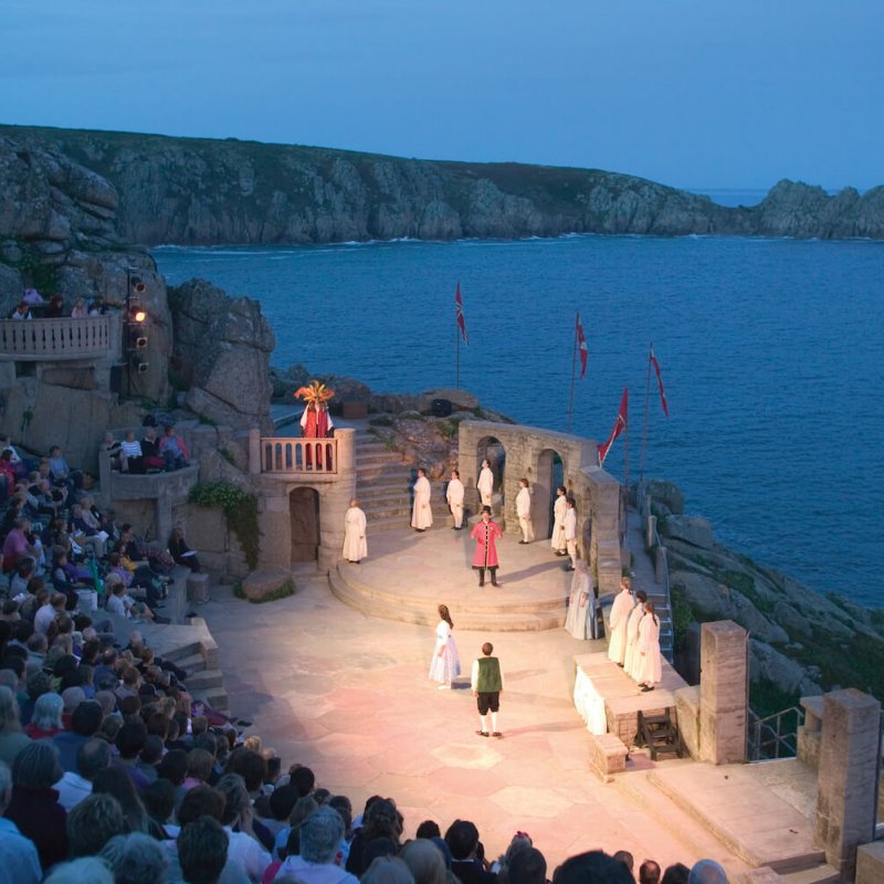 View of the Minack theatre at night, actors on the stage lit up against the dark sea.