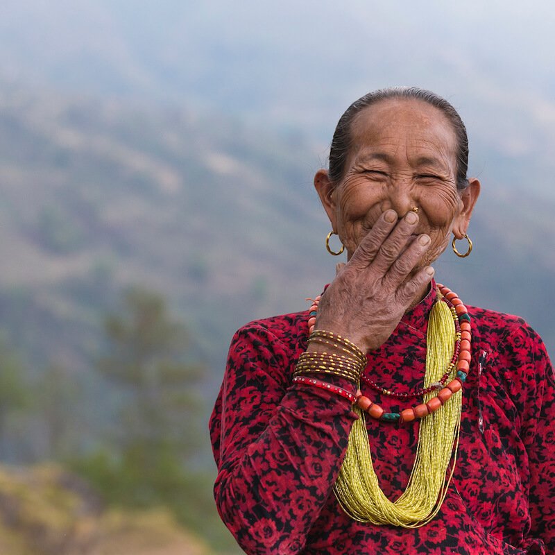 Asian woman laughing and holding hand to mouth.