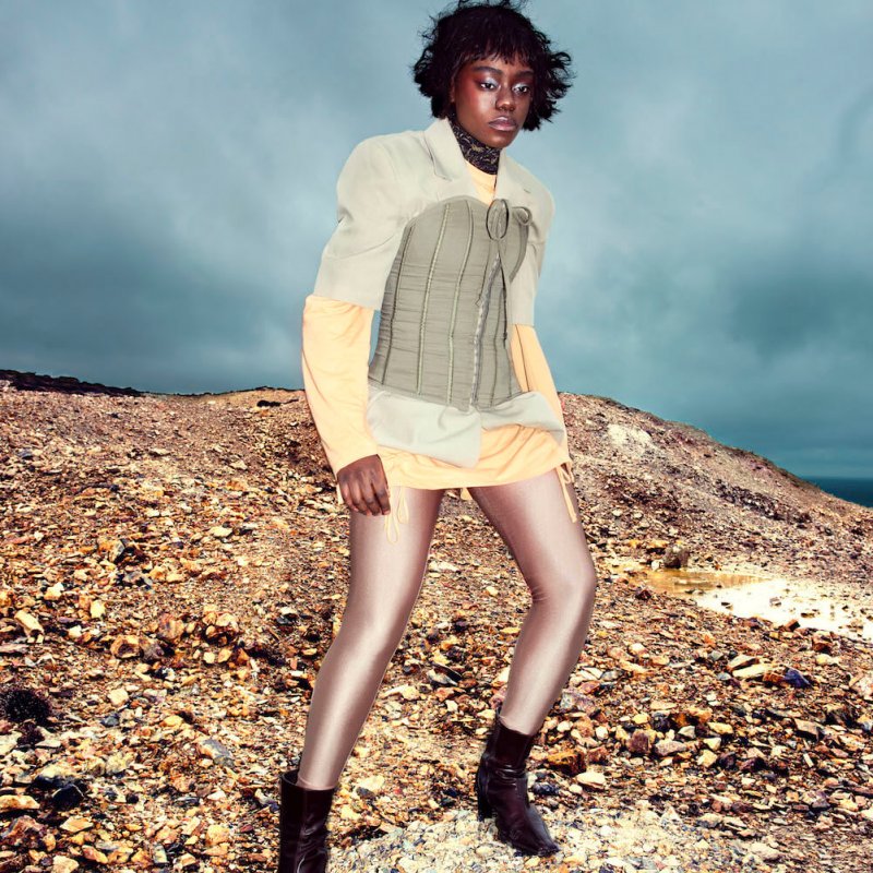 A person posing on a cliff top, wearing a jacket and boots