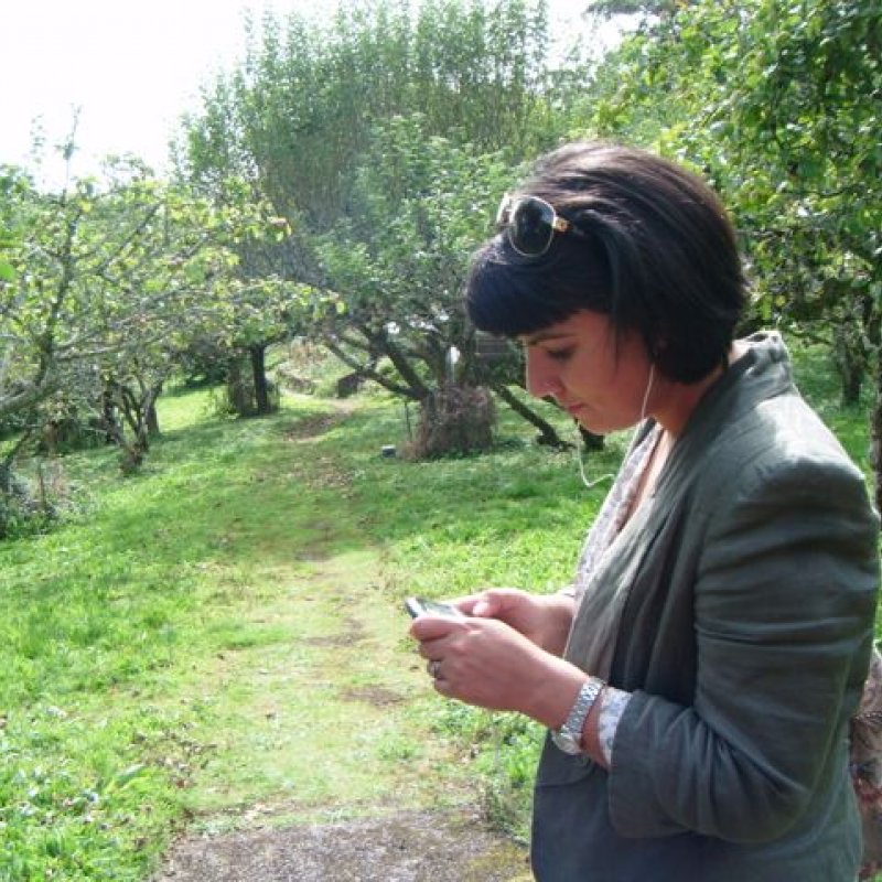 Female stood in a garden looking at device 