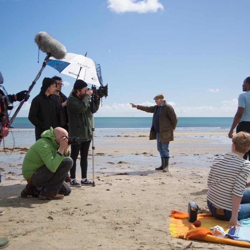 Film and TV students from Falmouth University filming a scene on a beach with blue sky