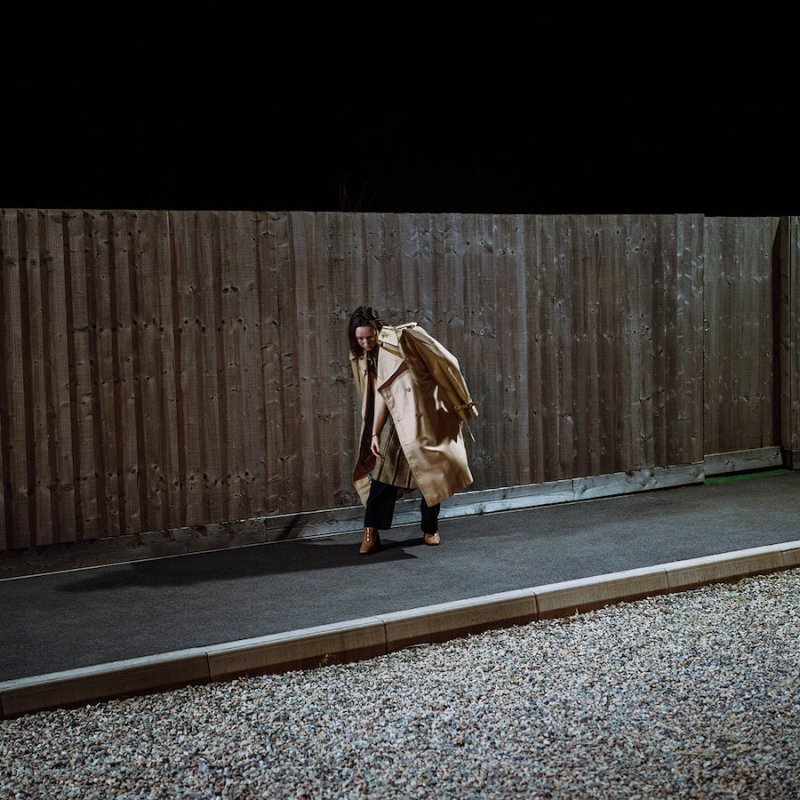 woman wearing a trench coat in front of a wooden fence