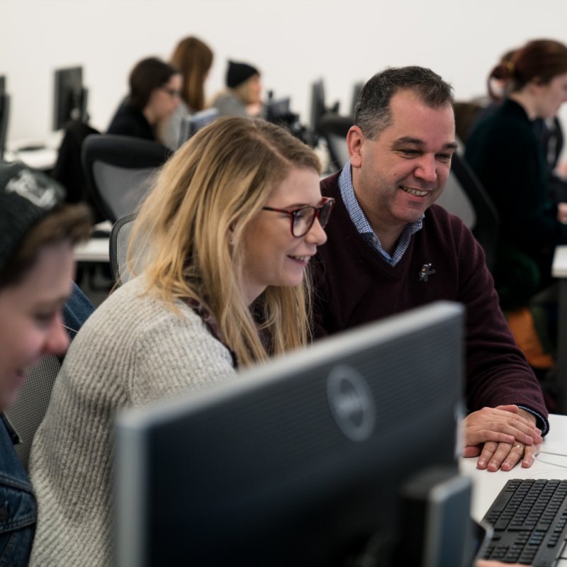 Student and lecturer working in room full of computers.