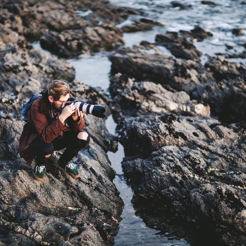Falmouth University Photography student sits on rocks photographing the sea