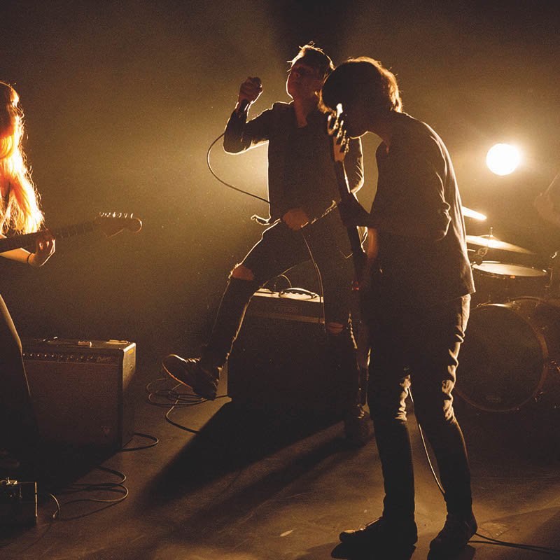 Four band members on stage, illuminated by a spotlight from behind them.