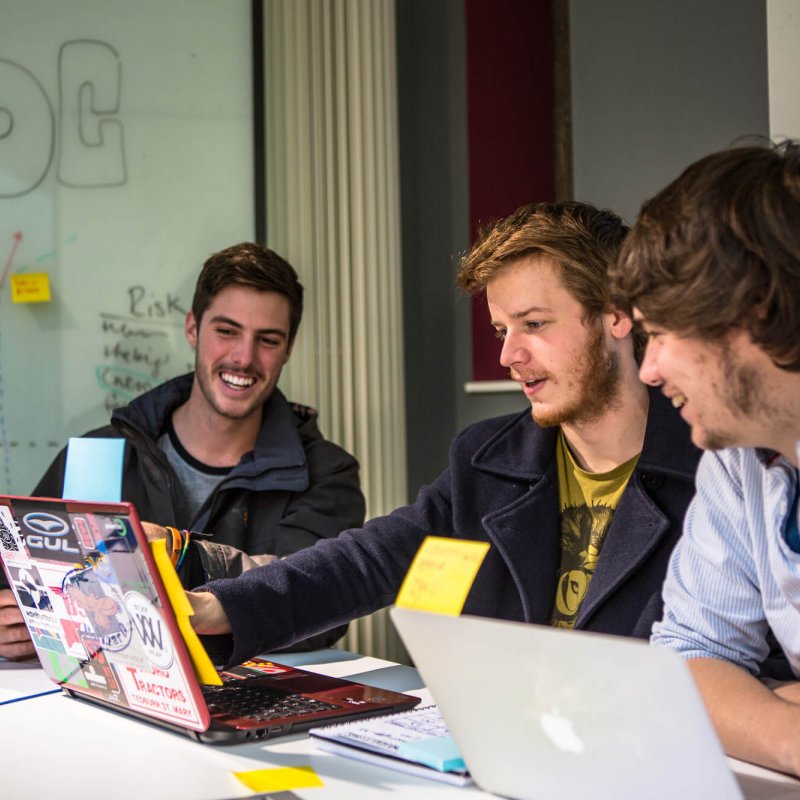 Falmouth University Business students smiling and looking at a laptop