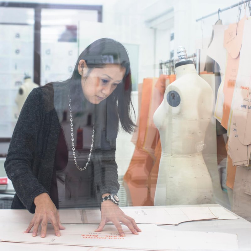 A Costume Design student at a mannequin with pattern cuttings hanging up