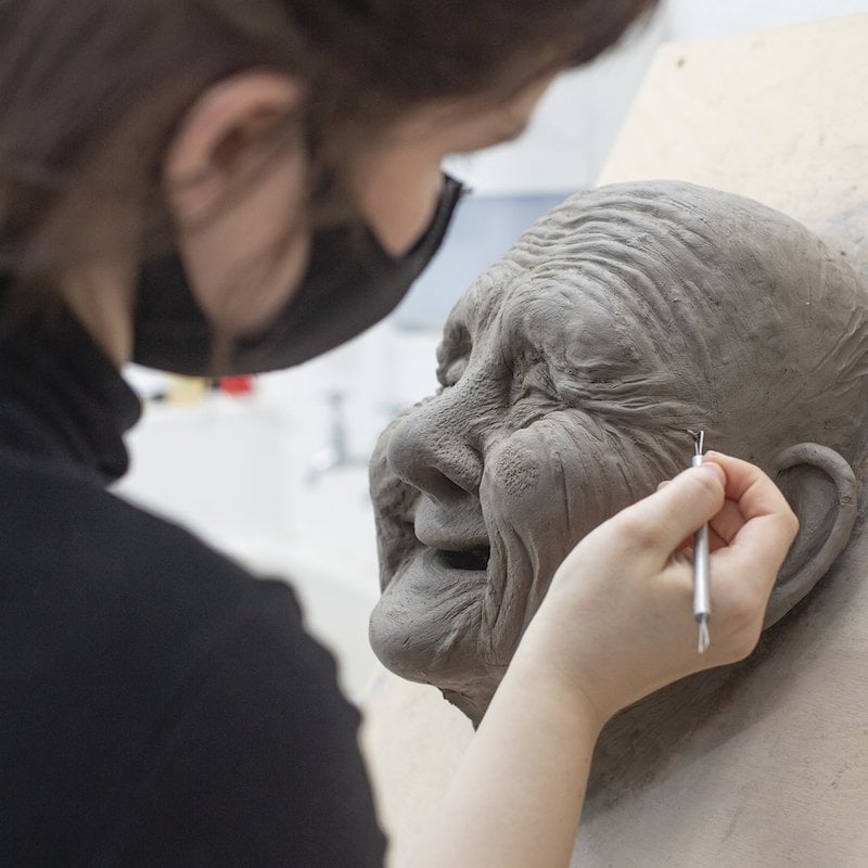 A student creating a clay model of an old woman
