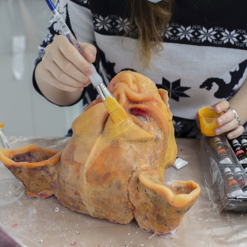 A student painting a monster's head with orange paint