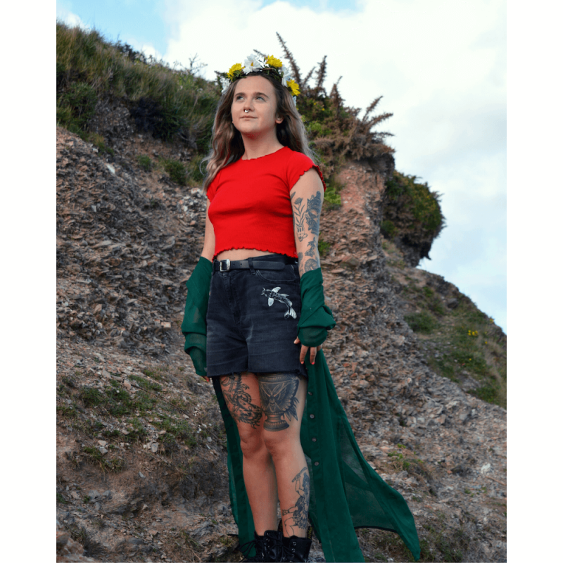 A woman wearing a red t-shirt and denim shorts designed by Falmouth University Fine Art graduate