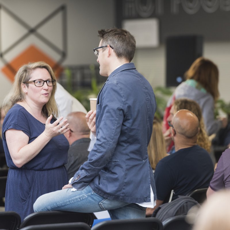 A man and a woman standing and talking in a room full of people