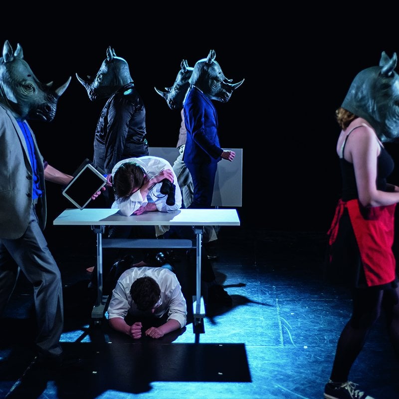 Actors wearing rhinoceros masks on stage.