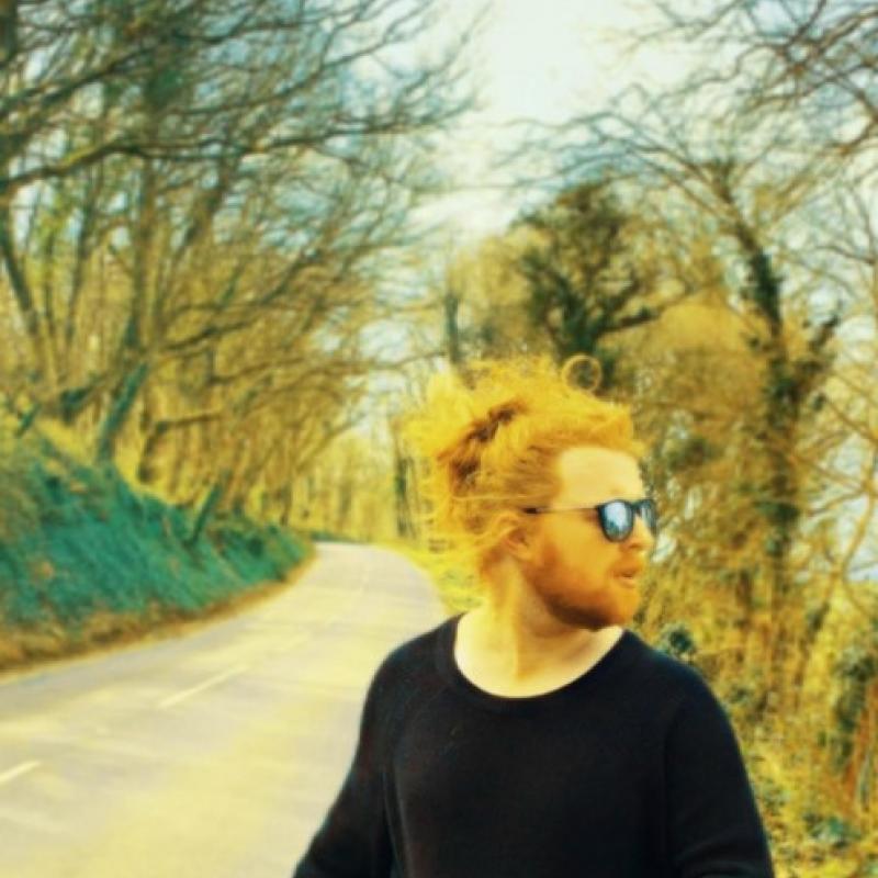 Man in black jumper poses by a forest