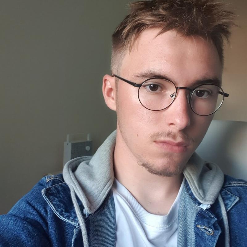 A male student wearing glasses and a denim jacket