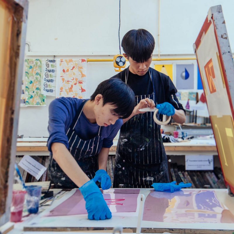 Two Falmouth University Graphic Design students screen printing in a studio