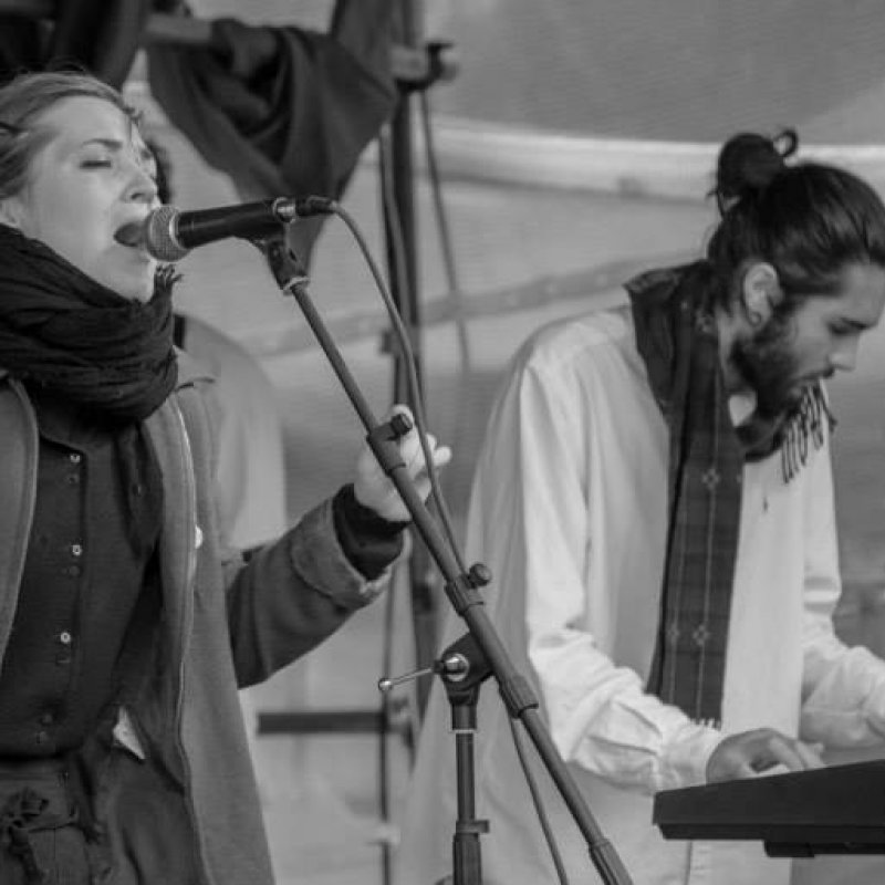 Musicians on stage singing into microphone and playing keyboard.