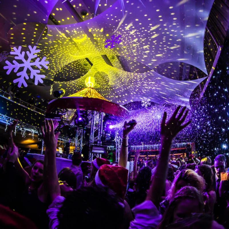 Dark room with disco lights and students dancing with arms in the air.