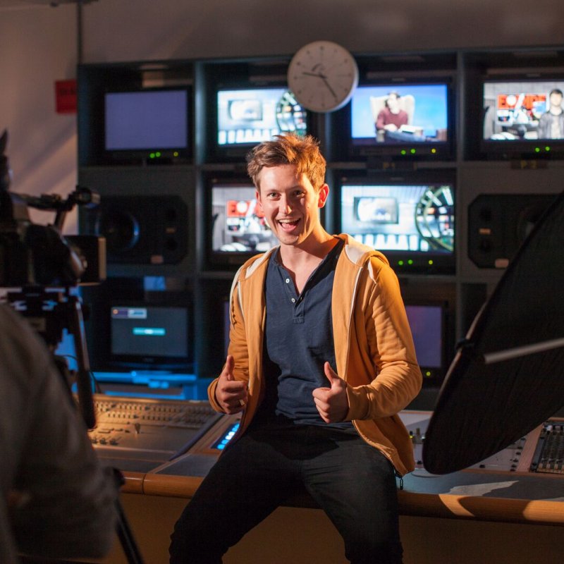 Student giving the thumbs up in television control studio.