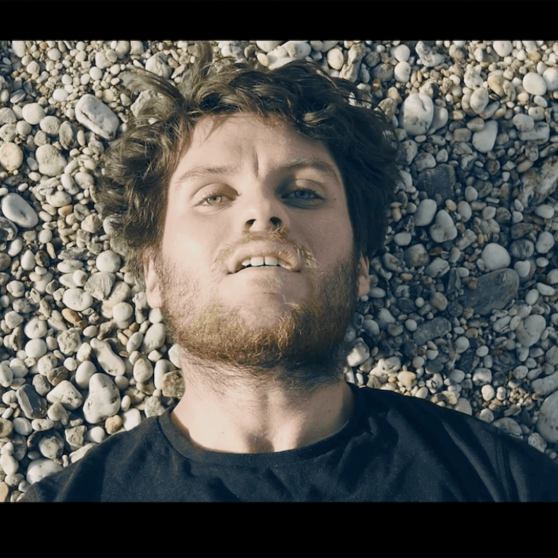 Shoulders and head shot of actor with beard lying on a beach.