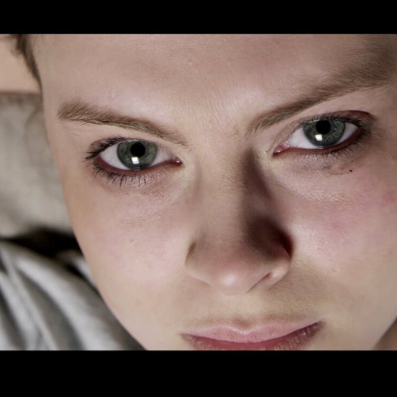 Film still of female staring into camera, makeup smudged.