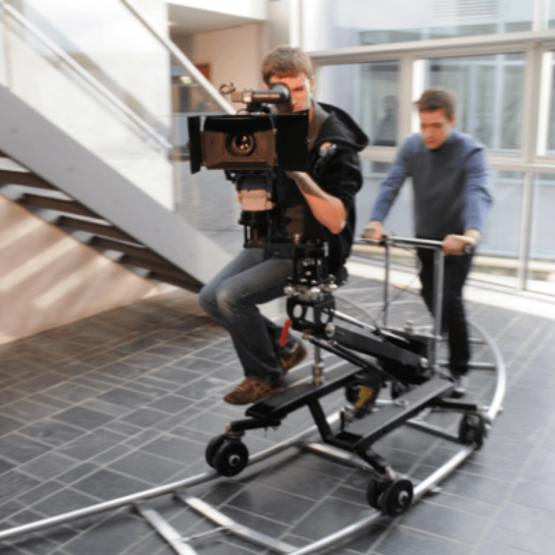Student behind camera on camera dolly being moved along a track.