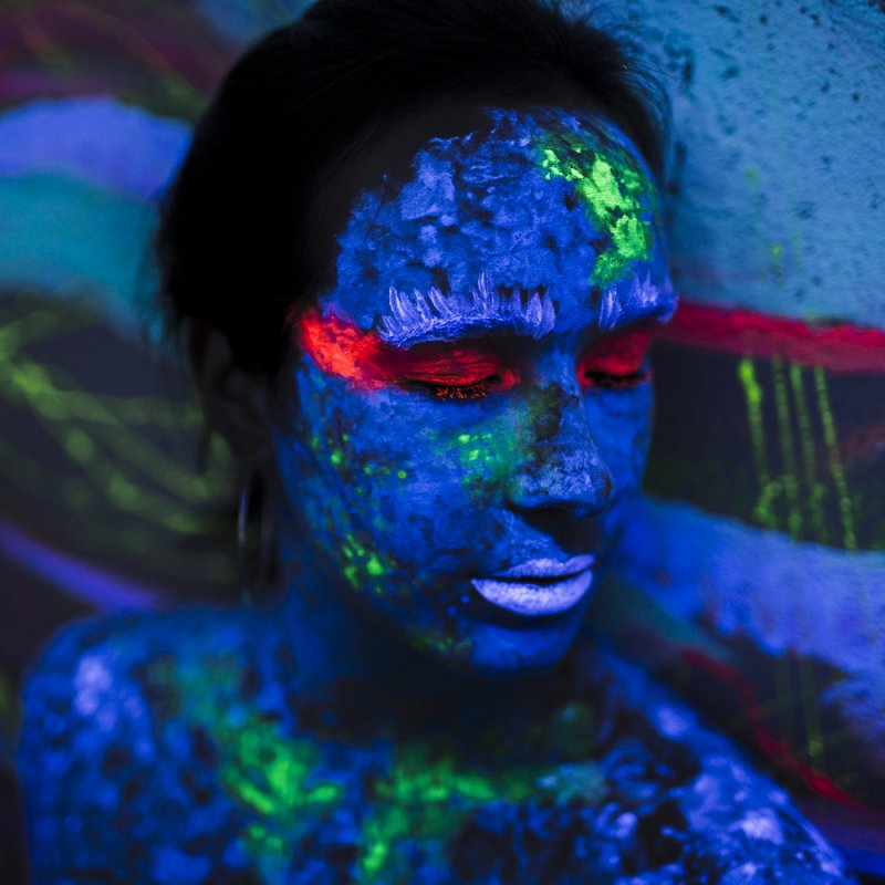 Lady with blue painted face and green and blue streaks on matching background.