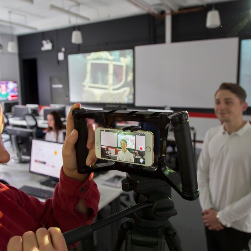 Student filming in the newsroom on a smartphone.