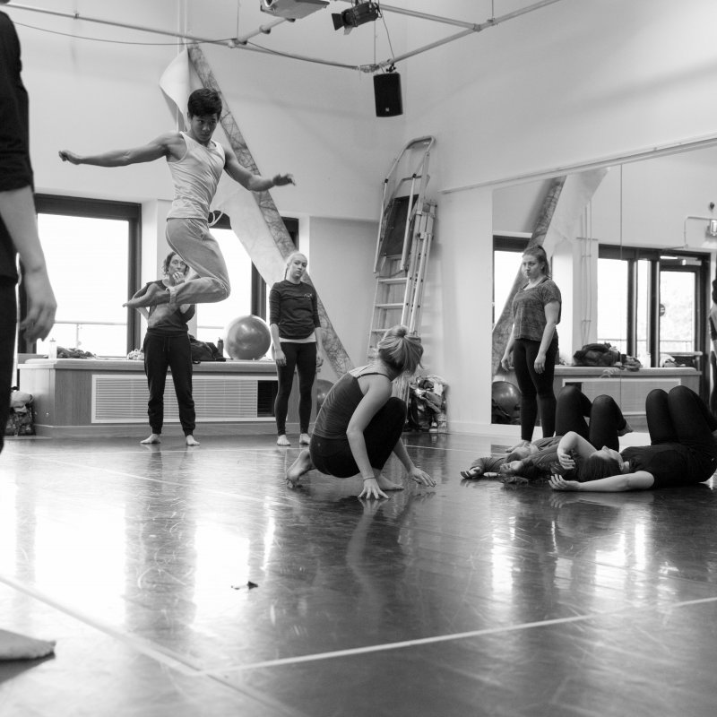 Student dancer jumping high and twisting dance studio as others look on.