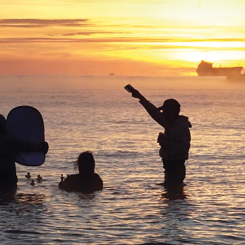 Falmouth University Film students waist deep in sea filming rubber ducks with sunrise