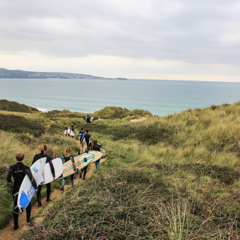 A line of Falmouth University students carrying surfboards heading to the beach