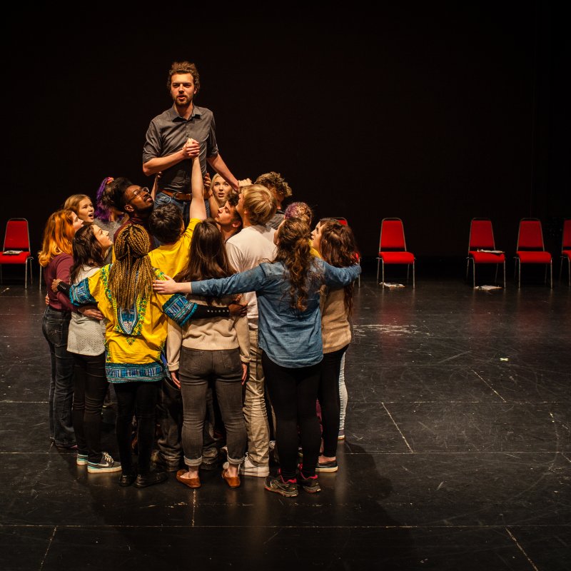 Group of student actors hugging in a circle with one actor raised up in the middle.