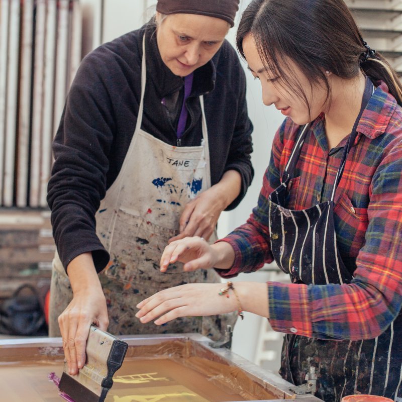 Female technician helping female student to screen print