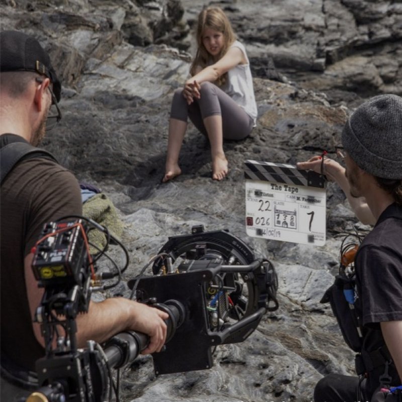 A girl is sitting on a rock being filmed by a camera crew