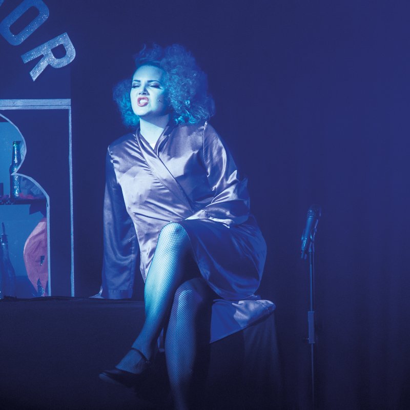 Actor in satin dressing gown singing and lit in blue light.