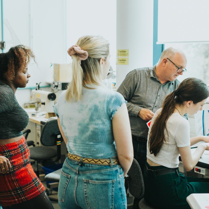 Students and teacher in textiles studio with one student at a sewing machine