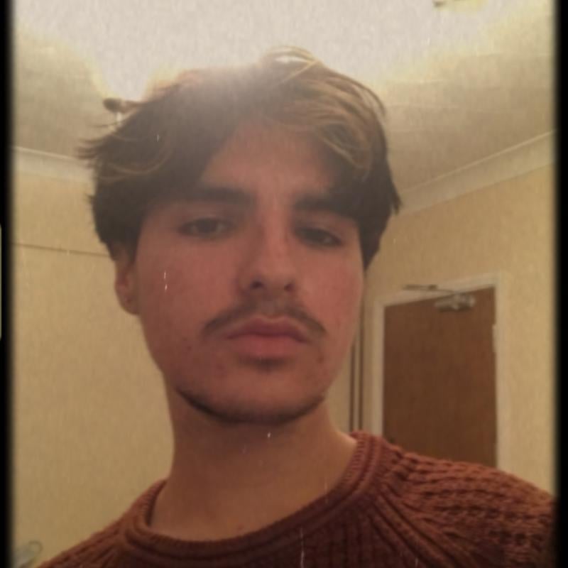 A Falmouth University student with a moustache, wearing a dark orange jumper