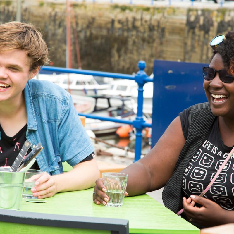 Two Falmouth University students seated at a table with glasses