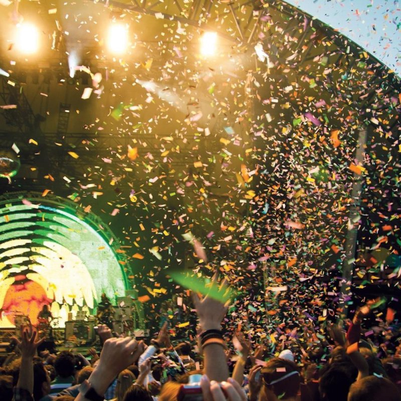 A large crowd with their hands in the air watching a music performance on a stage outside