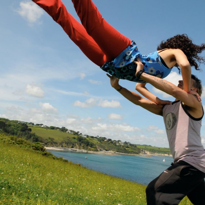 A male dancer lifting a female dancer high in the air on grass with the sea and sky in the background