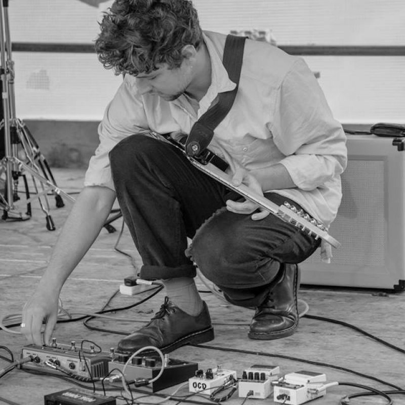 Guitarist on stage bending down and making adjustments to devices on the floor.