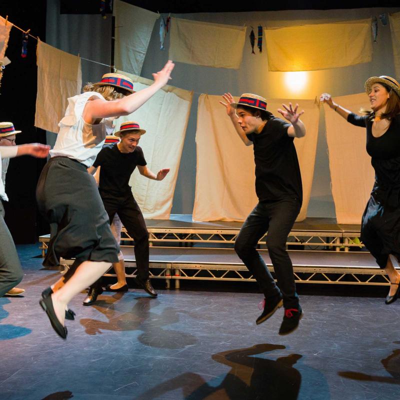 Falmouth University student actors wearing boater hats and jumping on stage