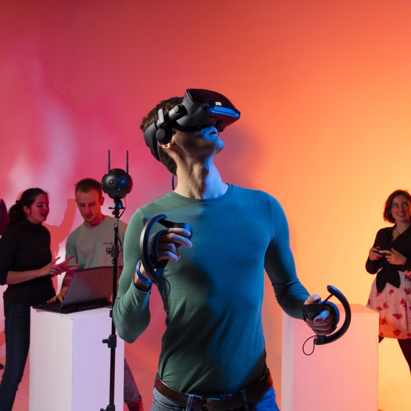 Games Academy students wearing a VR headset in front of an orange background