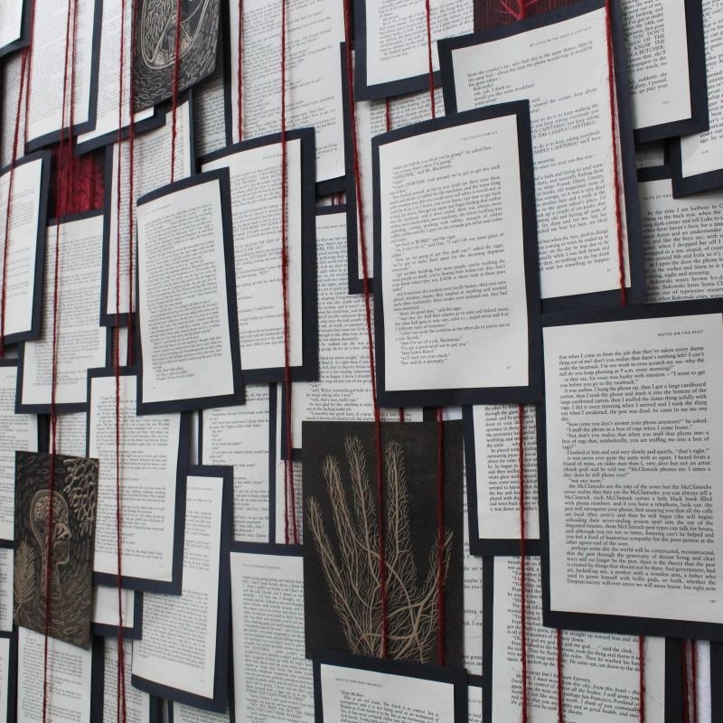 Many pages of black mounted text and images hanging on red strings.
