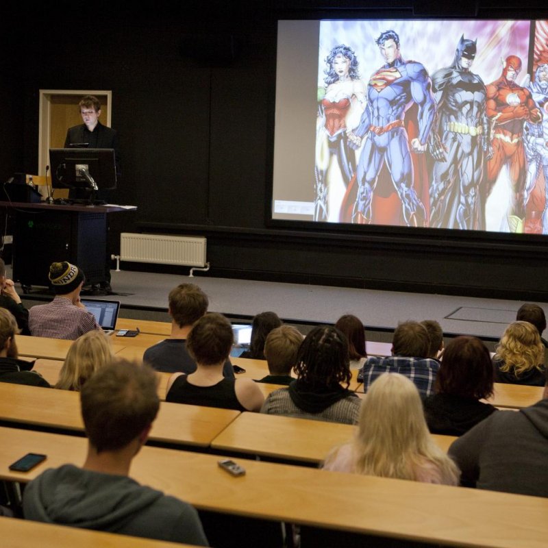 Dr Will Brooker talks with Film students, slide of Marvel characters in background.