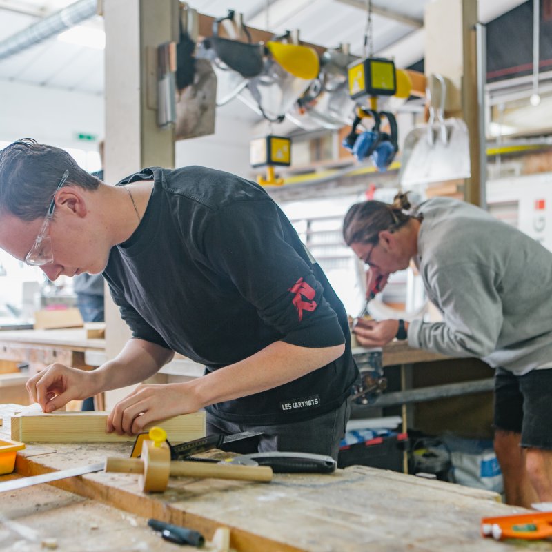 Male students wearing goggles working in a wood making workshop