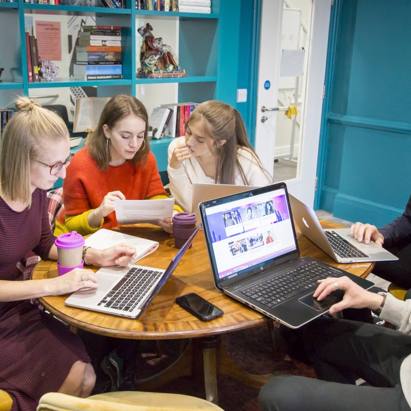 Students working at laptops in turquoise room with bookshelves.