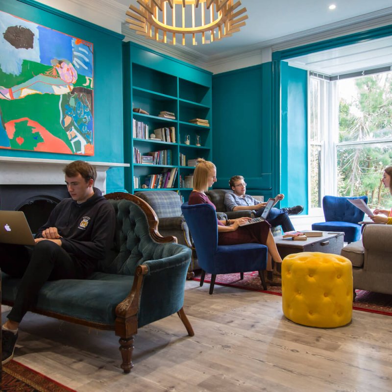 Falmouth University students sitting on armchairs and sofas in a teal room with wooden floor